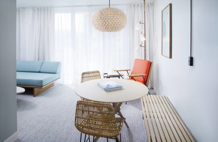 The Laylow, Autograph Collection: Gay-friendly hotel room interior with round table, rattan chairs, and a light blue sofa. Modern design.