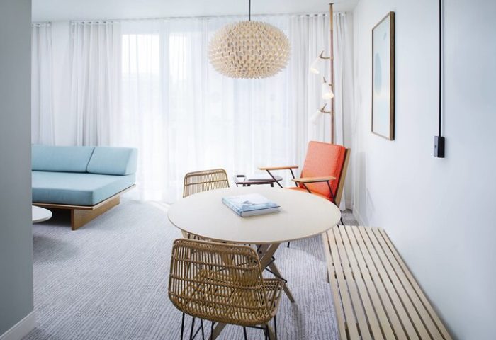 The Laylow, Autograph Collection: Gay-friendly hotel room interior with round table, rattan chairs, and a light blue sofa. Modern design.