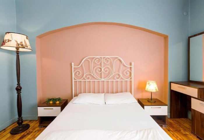 Cheers Midtown Hostel gay-friendly hotel room. White bed, peach accent wall, and blue walls. Nightstands, lamps, and dresser. Gay travel advice.