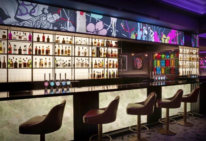 NYX Hotel London Holborn bar. Gay-friendly hotel interior with liquor shelves, colorful art, and bar stools. A stylish spot for gay men travelers.