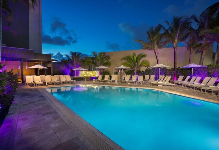 Sonesta Fort Lauderdale Beach gay-friendly hotel pool at night. Lounge chairs and palm trees surround the illuminated pool. Relaxing vacation.