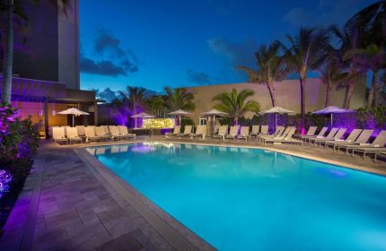 Sonesta Fort Lauderdale Beach gay-friendly hotel pool at night. Lounge chairs and palm trees surround the illuminated pool. Relaxing vacation.