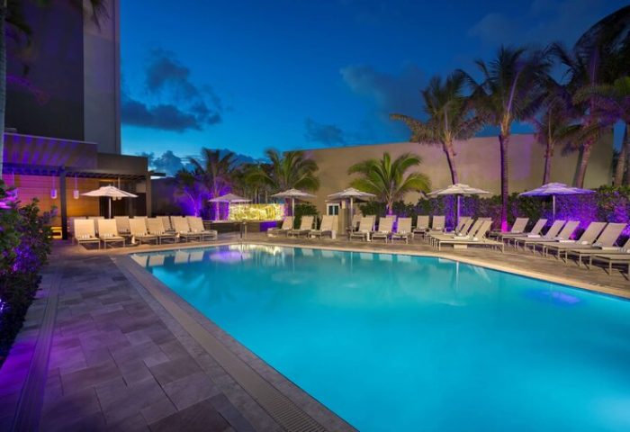 Sonesta Fort Lauderdale Beach gay-friendly hotel pool at night. Lounge chairs and palm trees surround the illuminated pool. Relaxing vacation.