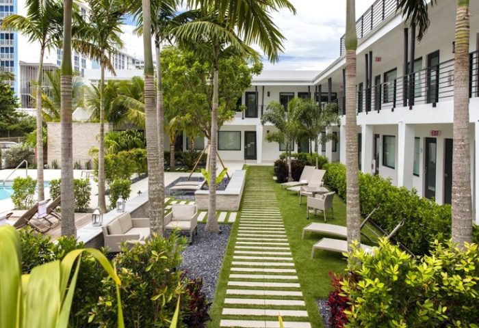 Elita Hotel's courtyard, a gay-friendly hotel. Lush greenery, palm trees, and modern architecture create a relaxing atmosphere. Ideal for gay travel.
