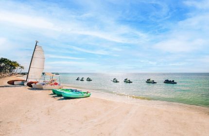 Casa Marina Key West beach scene. Sailboat and kayaks on sand. Jet skis on water. Gay-friendly hotel offers water sports.