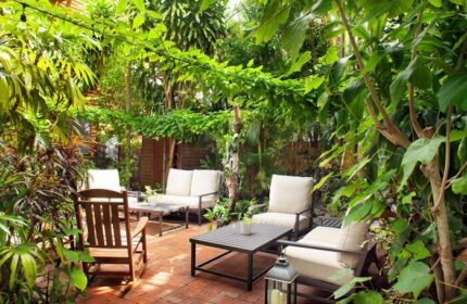 Island City House gay-friendly hotel courtyard. Lush tropical plants surround outdoor seating on a brick patio, creating a relaxing retreat.