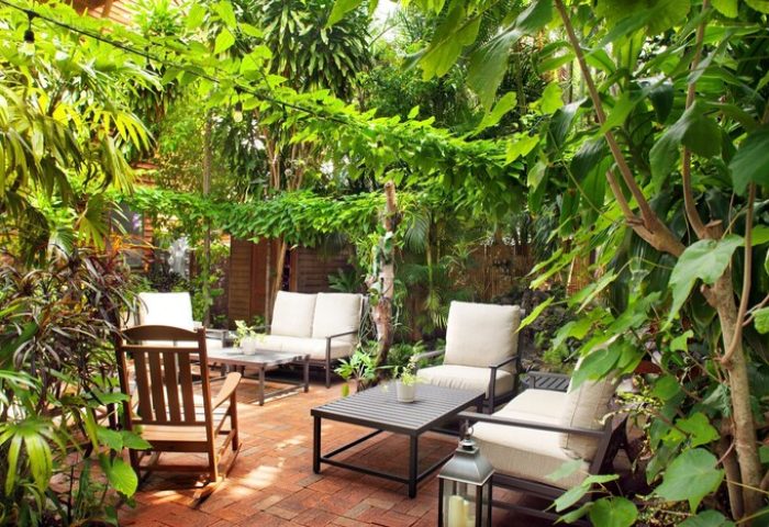 Island City House gay-friendly hotel courtyard. Lush tropical plants surround outdoor seating on a brick patio, creating a relaxing retreat.