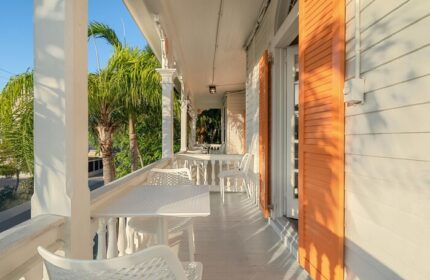 Balcony view at Marrero's Guest Mansion, a gay-friendly hotel. White tables, chairs, and orange shutters create a relaxing outdoor space.