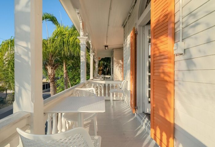Balcony view at Marrero's Guest Mansion, a gay-friendly hotel. White tables, chairs, and orange shutters create a relaxing outdoor space.