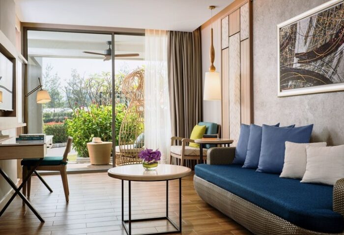 Avani+ Hua Hin Resort room. Gay-friendly hotel with a blue sofa, desk, and outdoor seating. Modern, bright, and inviting for gay travelers.