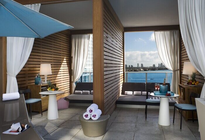 Kimpton EPIC Hotel gay-friendly suite. Balcony cabana with ocean view. Loungers, table, and towels. Luxury gay travel in Miami.