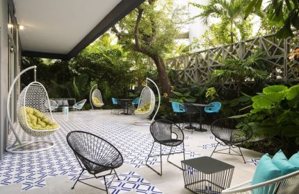 Hotel Indigo Miami Brickell gay-friendly hotel outdoor patio. Hanging chairs, modern furniture, lush greenery, and geometric tile floor.