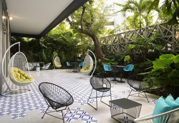 Hotel Indigo Miami Brickell gay-friendly hotel outdoor patio. Hanging chairs, modern furniture, lush greenery, and geometric tile floor.