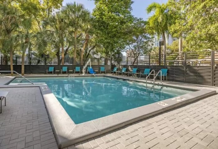 Pool at Comfort Inn & Suites Downtown Brickell-Port of Miami, a gay-friendly hotel. Turquoise chairs line the pool. Palm trees in background.