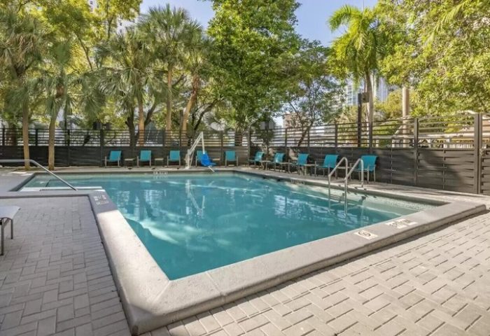 Pool at Comfort Inn & Suites Downtown Brickell-Port of Miami, a gay-friendly hotel. Turquoise chairs line the pool. Palm trees in background.