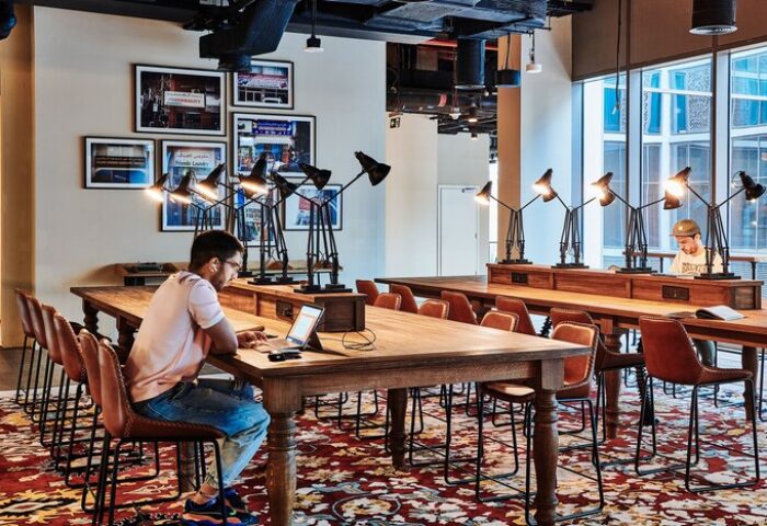 25hours Hotel One Central co-working space. Gay-friendly hotel with long tables, chairs, and lamps. Men work on laptops in a stylish setting.