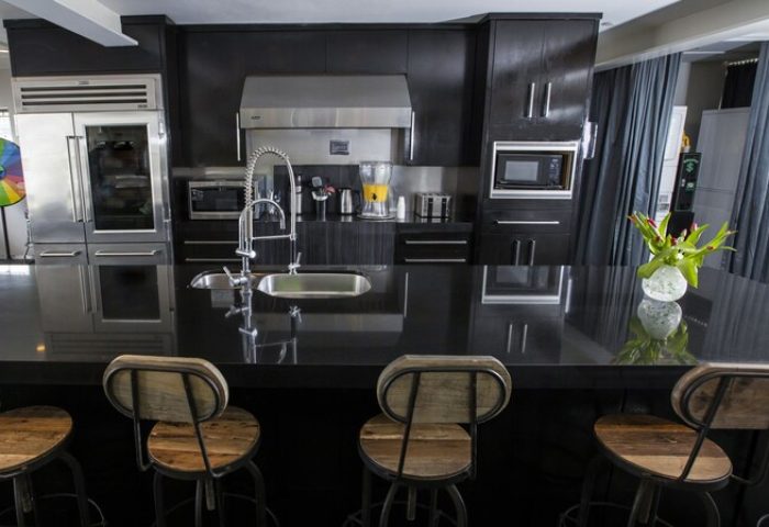 Posh South Beach gay-friendly hotel kitchen. Sleek black cabinets, stainless steel appliances, and counter with bar stools. Modern design.