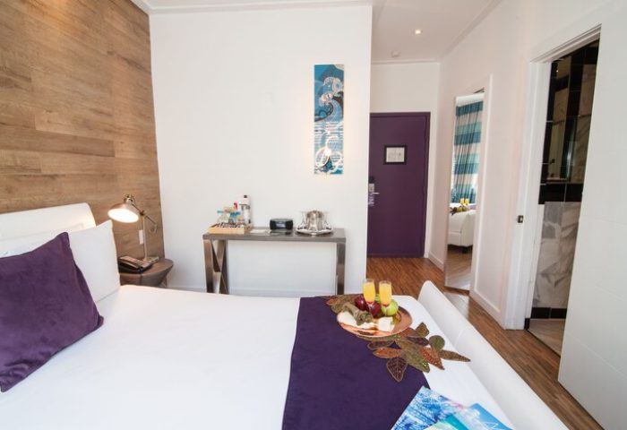 Hotel Shelley room: Gay-friendly hotel bedroom with king bed, wood accent wall, desk, and purple door. Modern design for gay men's travel.