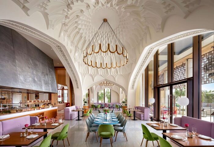 Atlantis The Royal gay-friendly hotel restaurant interior. Ornate ceiling, modern lighting, colorful seating. Gay travel advice.