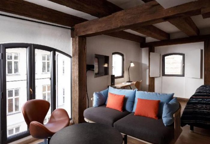 71 Nyhavn Hotel gay-friendly pet-friendly room. Beams, couch, chair, and desk. Hotel interior for gay men travel in Copenhagen, Denmark.