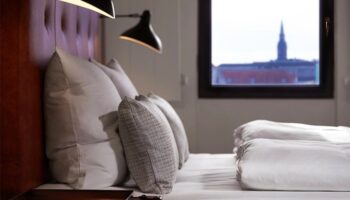 71 Nyhavn Hotel gay-friendly room. Pet-friendly hotel bedroom with pillows, lamps, and a window view. Luxury gay travel in Copenhagen.