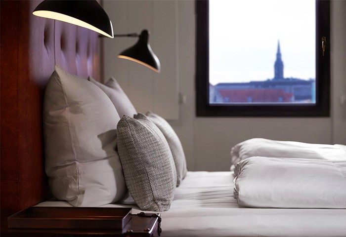 71 Nyhavn Hotel gay-friendly room. Pet-friendly hotel bedroom with pillows, lamps, and a window view. Luxury gay travel in Copenhagen.