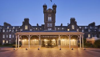 Crieff Hydro hotel exterior at dusk. Gay-friendly hotel with tower, entrance, and brick path. A great place for gay men to travel and visit.