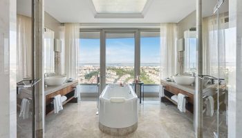 Raffles Istanbul Hotel bathroom with city view. Luxury gay-friendly hotel featuring a soaking tub, dual vanities, and floor-to-ceiling windows.