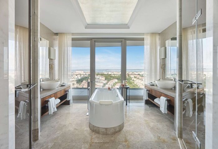 Raffles Istanbul Hotel bathroom with city view. Luxury gay-friendly hotel featuring a soaking tub, dual vanities, and floor-to-ceiling windows.