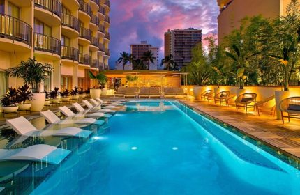 The Laylow, Autograph Collection gay-friendly hotel pool at dusk. Loungers are in the water, with seating on the deck. Tropical vibe.