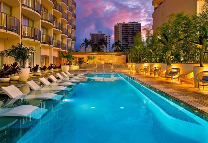 The Laylow, Autograph Collection gay-friendly hotel pool at dusk. Loungers are in the water, with seating on the deck. Tropical vibe.