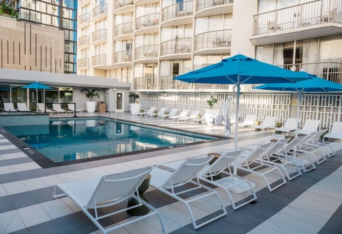 OHANA Waikiki East by OUTRIGGER pool view. Gay-friendly hotel in Honolulu with sun loungers and blue umbrellas. Relaxing travel destination.