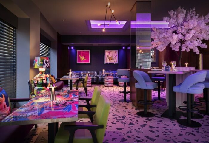 NYX Hotel London Holborn restaurant. Gay-friendly hotel dining area with colorful decor, bar stools, tables, and art. Modern design with purple lighting.