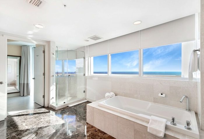 Hilton Fort Lauderdale Beach Resort gay-friendly hotel bathroom. Bathtub with ocean view, glass shower, and marble floor. Luxury travel.