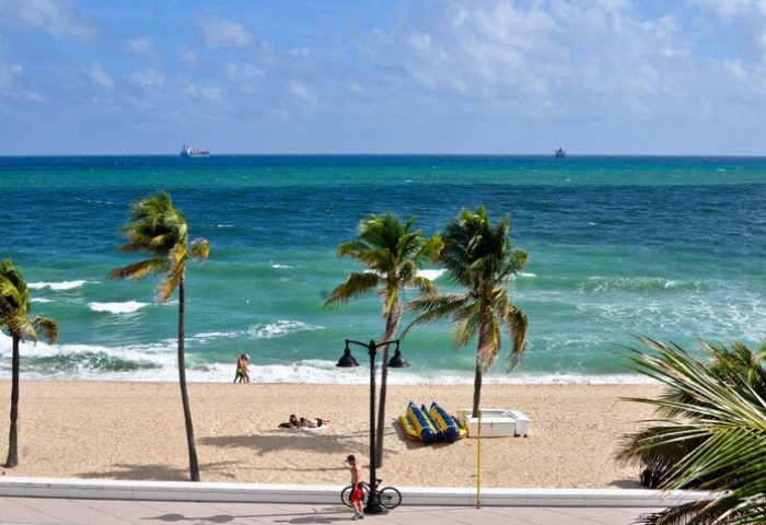 Gay-friendly hotel beach view. Palm trees, ocean, and beachgoers. Ideal gay travel destination. Relaxing scene for a gay vacation.