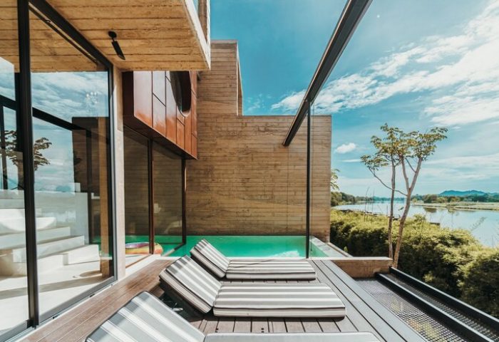 Cross River Kwai gay-friendly hotel. Deck with striped loungers, pool, and river view. Modern architecture, perfect for gay travel.