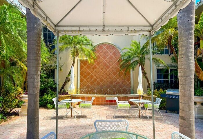 La Casa Hotel's gay-friendly courtyard. Outdoor seating area with palm trees, a fountain, and tropical vibes for gay men's travel.