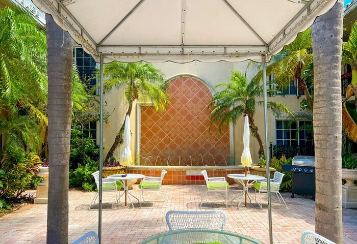 La Casa Hotel's gay-friendly courtyard. Outdoor seating area with palm trees, a fountain, and tropical vibes for gay men's travel.