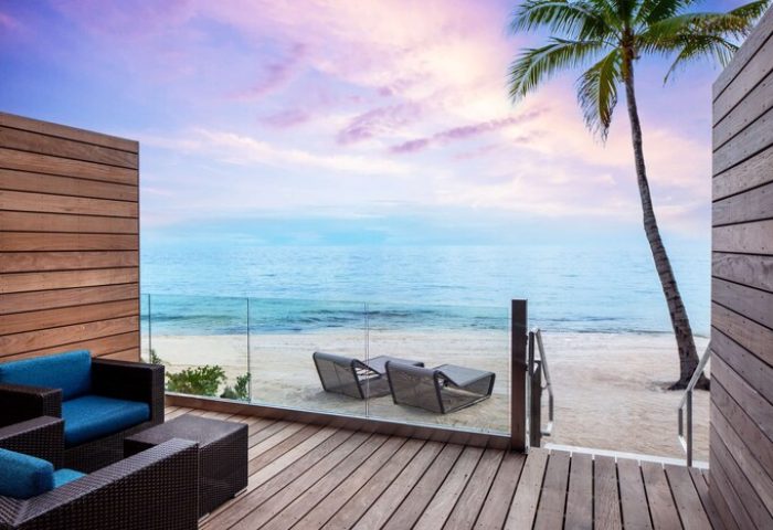 Casa Marina Key West hotel oceanfront view from a gay-friendly suite. Deck with lounge chairs, palm tree, & sunset. Curio Collection by Hilton.