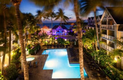 Opal Key Resort & Marina pool at night. Gay-friendly hotel with palm trees, ocean view, and illuminated buildings. Perfect for gay men's travel.