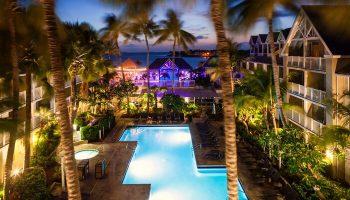 Opal Key Resort & Marina pool at night. Gay-friendly hotel with palm trees, ocean view, and illuminated buildings. Perfect for gay men's travel.