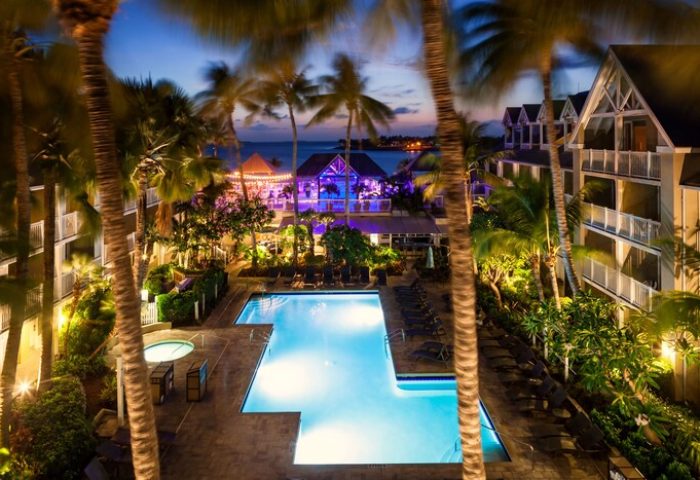 Opal Key Resort & Marina pool at night. Gay-friendly hotel with palm trees, ocean view, and illuminated buildings. Perfect for gay men's travel.