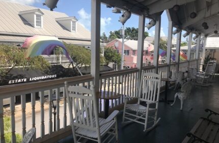 New Orleans house: Gay-friendly hotel porch with rocking chairs and rainbow flags. A welcoming spot for LGBTQ+ travelers.