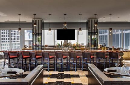 W Miami gay-friendly hotel bar area. High-rise view, bar stools, and a black and white checkered floor. Upscale gay travel destination.
