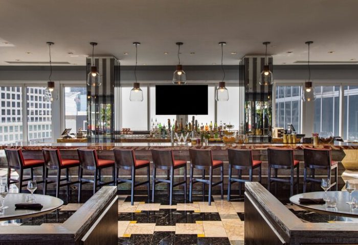 W Miami gay-friendly hotel bar area. High-rise view, bar stools, and a black and white checkered floor. Upscale gay travel destination.