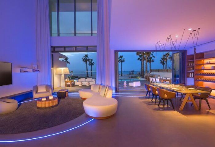 Nikki Beach Resort & Spa Dubai interior, a gay-friendly hotel. Modern living room with ocean view, palm trees. Luxury travel for gay men.