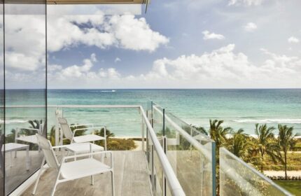 Four Seasons Hotel at The Surf Club balcony view. Oceanfront gay-friendly hotel with white chairs, tables, and glass railings overlooking the sea.