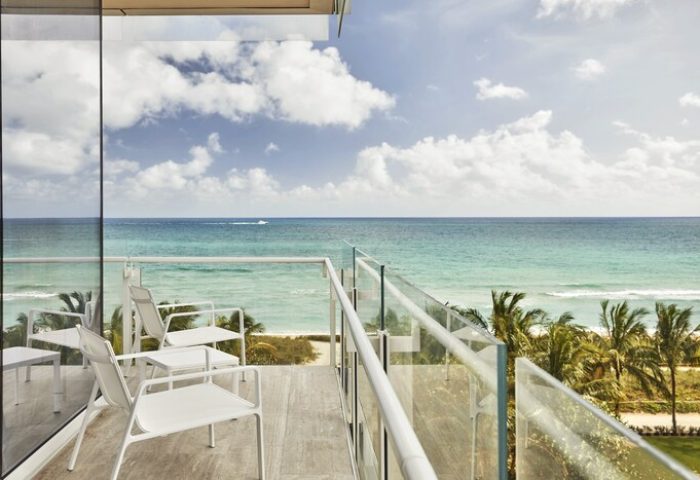 Four Seasons Hotel at The Surf Club balcony view. Oceanfront gay-friendly hotel with white chairs, tables, and glass railings overlooking the sea.