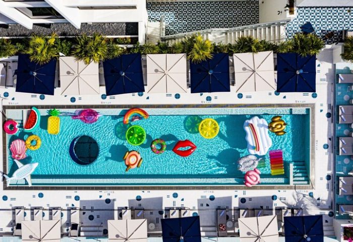 Aerial view of Moxy Miami South Beach Hotel pool with colorful floats. Gay-friendly hotel pool scene with umbrellas and lounge chairs.