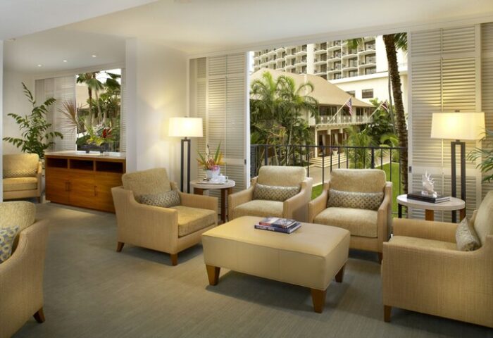 Halekulani Hotel living room. Gay-friendly hotel lounge area with armchairs, lamps, and a view of the tropical garden. Luxury travel in Honolulu.